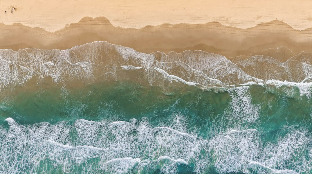 Aerial view of a golden coastline with turquoise ocean waves at sunset